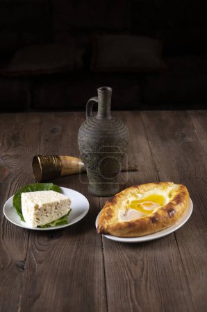 Photo for Wine in an amphora, a horn glass, cheese pie eggplant rolls, cheese and sesame seeds on a wooden table. Traditional Georgian feast - Royalty Free Image