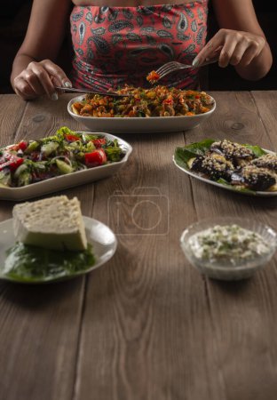Téléchargez les photos : Femme manger plat d'entrée traditionnel arménien, turc et grec sur une table en bois. - en image libre de droit