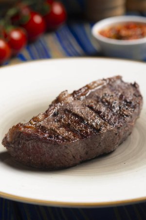 Téléchargez les photos : Steak rôti, tomates cerises, sel et poivre sur table en bois bleu. - en image libre de droit