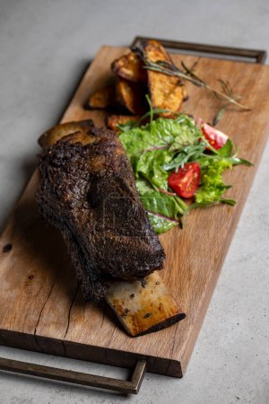 Photo for Roasted veal rib with baked potatoes and vegetables on a wooden board - Royalty Free Image