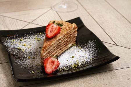Photo for Layer sponge cake with strawberries on a black plate on wooden background - Royalty Free Image