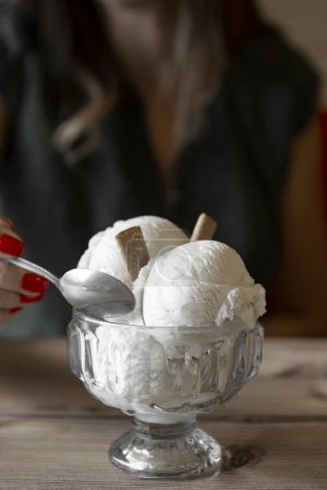 Téléchargez les photos : Gros plan de crème glacée dans un bol en verre avec cuillère dans les mains féminines .ice crème dans un bol en verre sur une table en bois - en image libre de droit
