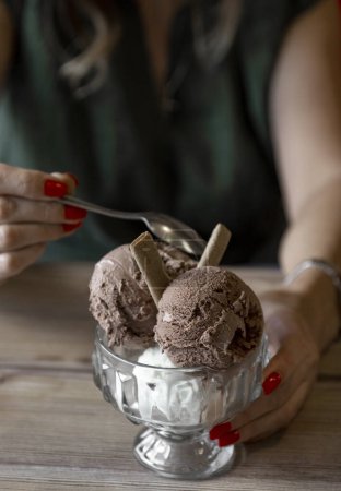 Photo for Close-up of ice cream in glass bowl with spoon in female hands .ice cream in a glass bowl on a wooden table - Royalty Free Image
