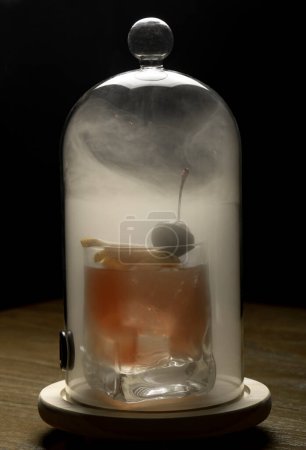 Foto de Cóctel en una copa con humo sobre una mesa de madera. - Imagen libre de derechos