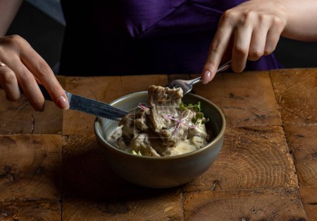 Téléchargez les photos : Femme manger rack d'agneau dans une sauce à la crème avec pomme et radis dans un bol - en image libre de droit