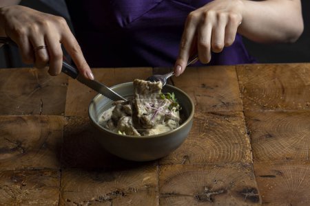 Téléchargez les photos : Femme manger rack d'agneau dans une sauce à la crème avec pomme et radis dans un bol - en image libre de droit