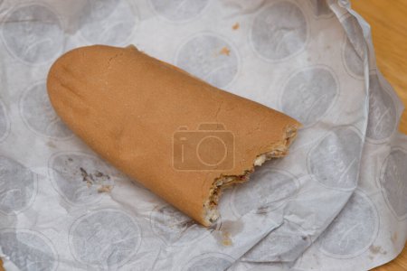 Téléchargez les photos : Gros plan d'un sandwich à moitié mangé sur du papier blanc. Concentration sélective et faible profondeur de champ. - en image libre de droit