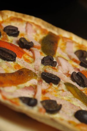 Foto de Pizza con jamón, tomate y aceitunas sobre fondo negro - Imagen libre de derechos