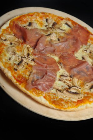 Foto de Pizza con jamón, champiñones y queso en un plato de madera. - Imagen libre de derechos
