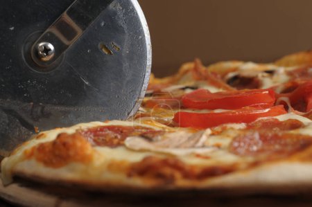Téléchargez les photos : Process of cutting pizza with ham, cheese and tomatoes on a wooden board. - en image libre de droit
