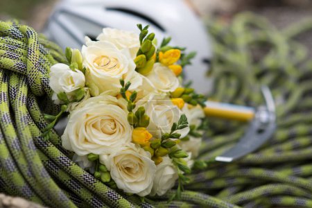 Téléchargez les photos : A wedding bouquet of white roses with gold hoops placed on a rope with an ice axe - en image libre de droit