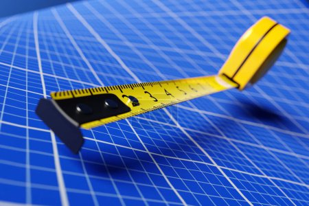 Foto de Ilustración 3D de una cinta métrica amarilla sobre un fondo de papel gráfico azul. Instrumento de medición manual para trabajos de construcción, renovación o carpintería. - Imagen libre de derechos