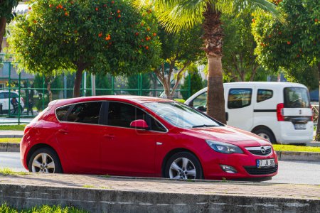 Foto de Side, Turkey -January 21, 2023: red Opel Astra está estacionado en la calle en un día cálido con el telón de fondo de un edificio, árboles, tiendas - Imagen libre de derechos