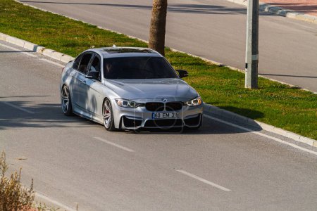 Foto de Side, Turkey -January 22, 2023: silver BMW 3-series está conduciendo rápido en la calle en un cálido día de verano con el telón de fondo de una palma - Imagen libre de derechos