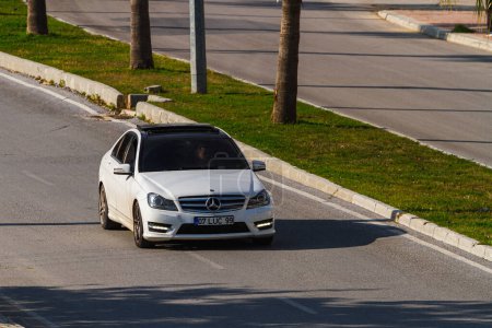 Téléchargez les photos : Side, Turkey -January 22, 2023:   white Mercedes-Benz C-class   is driving fast   on the street on a  summer day against the backdrop of a palms - en image libre de droit