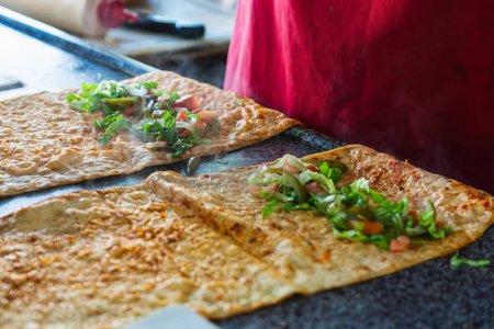 Foto de We cook shawarma step by step: a large round pita bread is spread with  chicken, salad and tomato on a wooden board. Cooking fast food. - Imagen libre de derechos