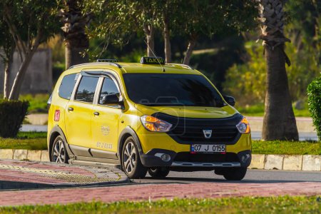 Téléchargez les photos : Côté, Turquie -23 janvier 2023 : taxi jaune Dacia Lodgy roule vite dans la rue par une chaude journée d'été sur fond de palmiers - en image libre de droit