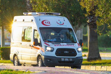 Foto de Side, Turkey -January 23, 2023: ambulancia blanca Ford conduciendo en la calle en un cálido día de verano con el telón de fondo del estacionamiento. - Imagen libre de derechos