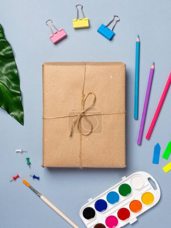 Photo for Gift books wrapped in recycled paper and tied with a rope, pens, pencils, stationery on a blue background. Flat lay, top view. - Royalty Free Image