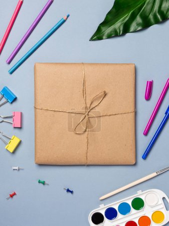 Photo for Gift books wrapped in recycled paper and tied with a rope, pens, pencils, stationery on a blue background. Flat lay, top view. - Royalty Free Image