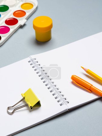 Photo for Top view arrangement with notepad with white sheets and pens, pencils, paper clips and other office supplies on blue background - Royalty Free Image