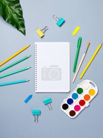 Photo for Top view arrangement with notepad with white sheets and pens, pencils, paper clips and other office supplies on blue background - Royalty Free Image