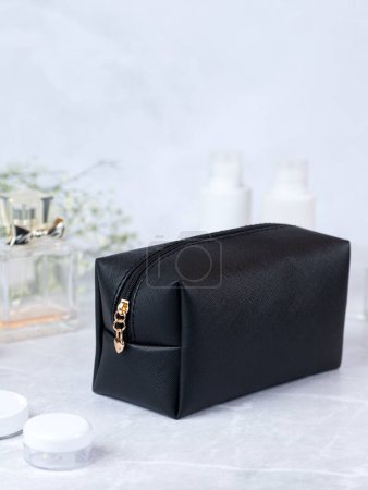 Foto de Accesorios de baño, bolsa de aseo. Bolso cosmético negro con cremallera con flores y perfume en el fondo - Imagen libre de derechos
