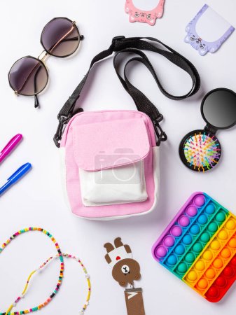Photo for Flat lay photo of baby bag with cosmetics, cosmetics and smartphone, pop it toys, key chain sunglasses top view of basic beauty items for girl - Royalty Free Image