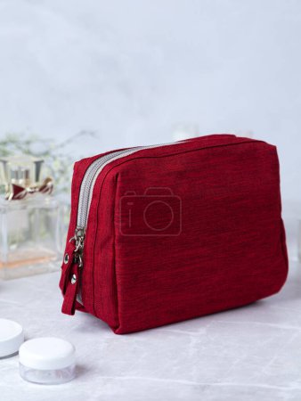 Photo for Red cosmetic bag  on a stone table, with flowers and perfume in the background - Royalty Free Image