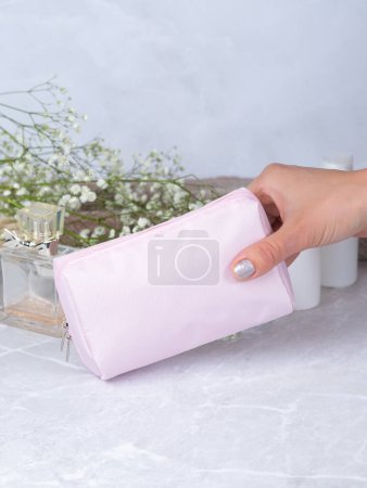 Téléchargez les photos : Sac cosmétique en cuir blanc sur une table en pierre, avec fleurs et parfum en arrière-plan - en image libre de droit