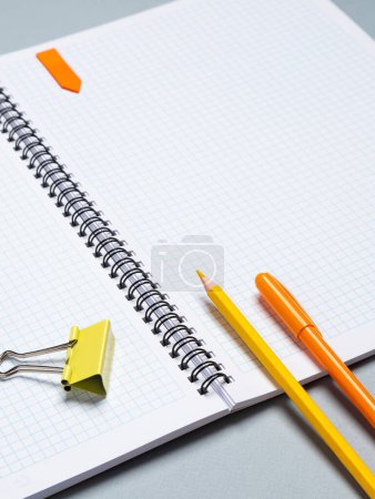 Foto de Primer plano de un cuaderno de papel con hojas en blanco, una pluma, un lápiz y un clip de papel sobre un fondo azul - Imagen libre de derechos