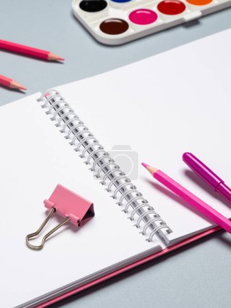 Photo for A schoolchild's workplace with an open notebook, pencils, pens, brushes, watercolors and other stationery on a light table - Royalty Free Image