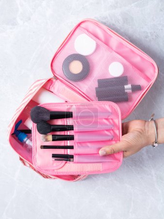 Foto de Una hermosa bolsa de cosméticos rosa con los productos necesarios para el cuidado de la piel de las mujeres. Cosméticos, champú, cremas, cepillos de maquillaje en una bolsa de cosméticos contra el telón de fondo de un hermoso baño de mujeres. - Imagen libre de derechos