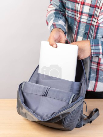 Téléchargez les photos : Un homme emballe son ordinateur portable dans un sac à dos, gros plan - en image libre de droit