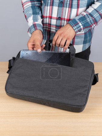 Photo for A man in a plaid shirt takes out a black notebook from a stylish backpack for work - Royalty Free Image