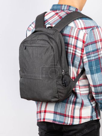 Photo for Close-up of a young student in a plaid shirt with a gray backpack for study and work on a light background - Royalty Free Image