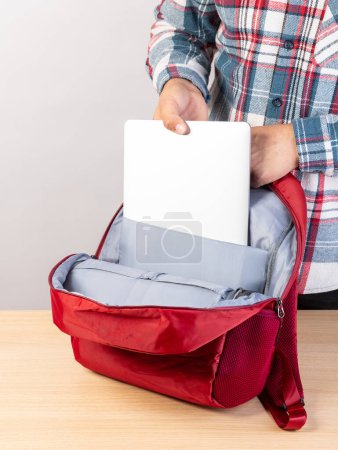 Close-up of a young male student taking out a laptop from a backpack.