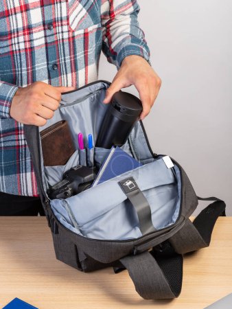 Téléchargez les photos : Un homme en chemise à carreaux sort une tasse de café d'un sac à dos élégant - en image libre de droit