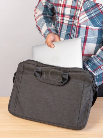 Foto de Un hombre pone un portátil en una bolsa afuera, sobre un fondo claro. Un joven mete un portátil en una mochila. Un hombre saca un portátil de su mochila. - Imagen libre de derechos
