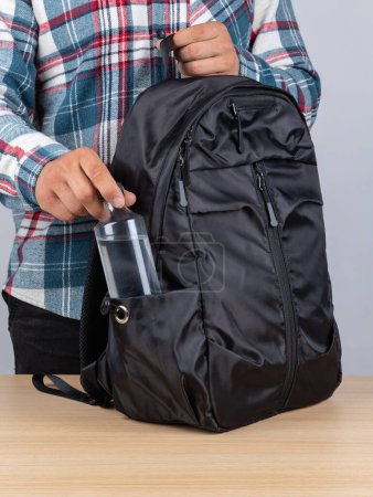 Foto de Primer plano de un joven estudiante sacando una botella de agua de su mochila. - Imagen libre de derechos