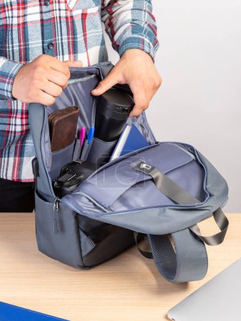 Foto de Primer plano de un joven estudiante sacando una taza de café de una mochila que también contiene una computadora portátil, billetera, bloc de notas - Imagen libre de derechos