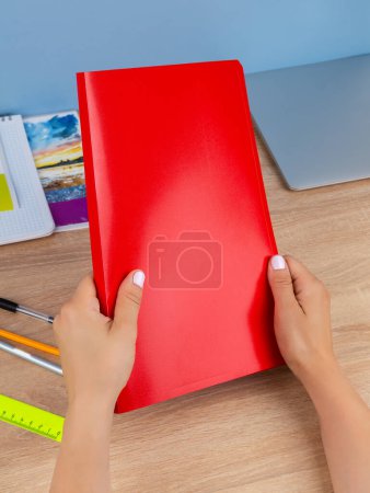 Foto de Primer plano de las manos de una mujer sosteniendo documentos en una manga en una carpeta de plástico rojo sentada en casa sobre la mesa - Imagen libre de derechos