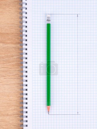 Photo for Close-up of a green  slate pencil lying on a checkered notebook, ready to start work - Royalty Free Image
