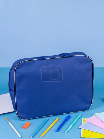 Photo for Blue  briefcase folder for documents and school items on a bright blue table next to stationery - Royalty Free Image