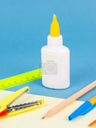 Photo for Glue bottle next to various office supplies, isolated on blue background, closeup - Royalty Free Image