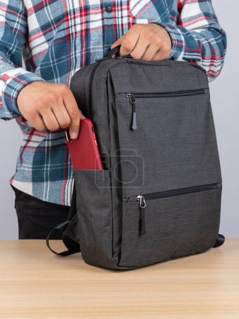 Photo for A man in a plaid shirt takes out a phone  from a stylish backpack for work - Royalty Free Image