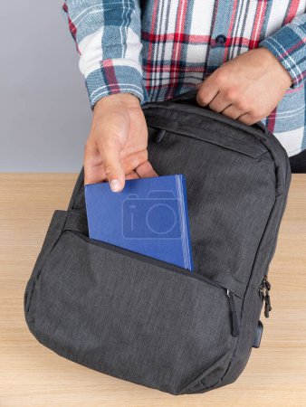 Photo for A man in a plaid shirt takes out a blue notebook from a stylish backpack for work - Royalty Free Image