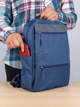 Photo for A man in a plaid shirt takes out a phone  from a stylish backpack for work - Royalty Free Image