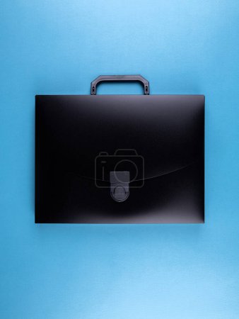 Photo for Black plastic  briefcase folder for documents and school items on a bright blue table - Royalty Free Image