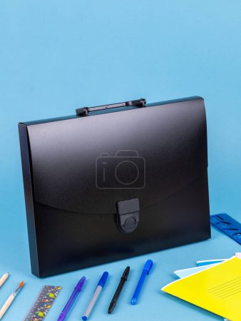 Téléchargez les photos : Porte-documents en plastique noir pour documents et articles scolaires sur une table bleu vif à côté de la papeterie - en image libre de droit